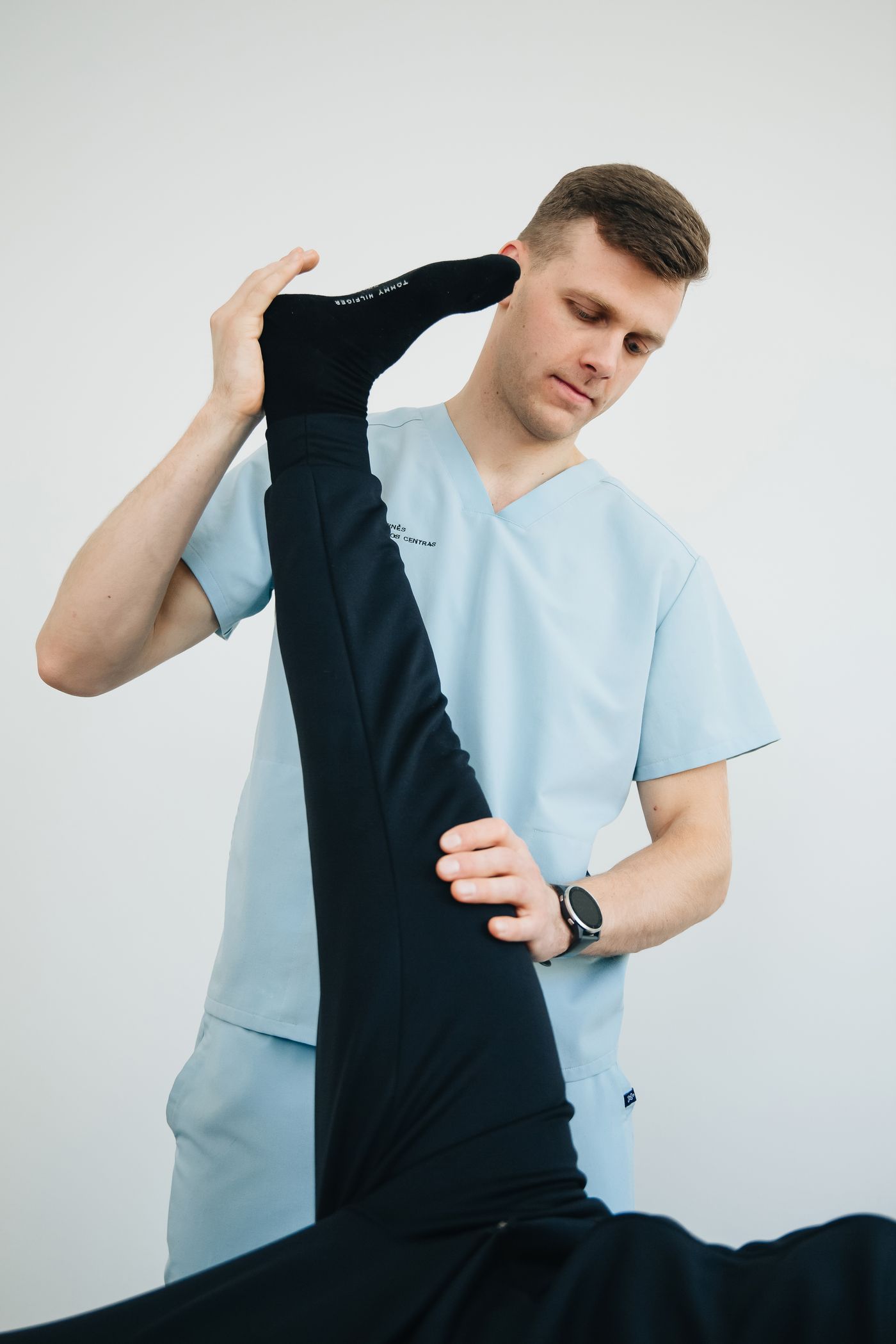 Physiotherapist in blue scrubs guiding a patient through a leg stretch during an in-home physiotherapy session